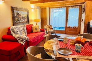 A cozy room with a red sofa, a dining table with a red tablecloth, and a painting on the wall.