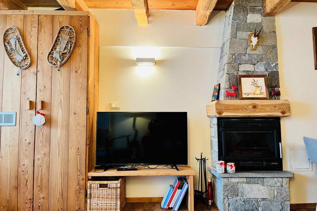 A living room with a TV, fireplace, wooden walls, and a stone fireplace surround.