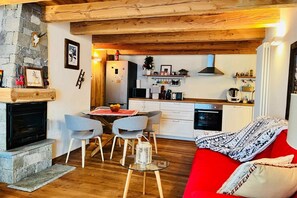 A cozy living room with a fireplace, a red sofa, and a dining area with chairs and a table.