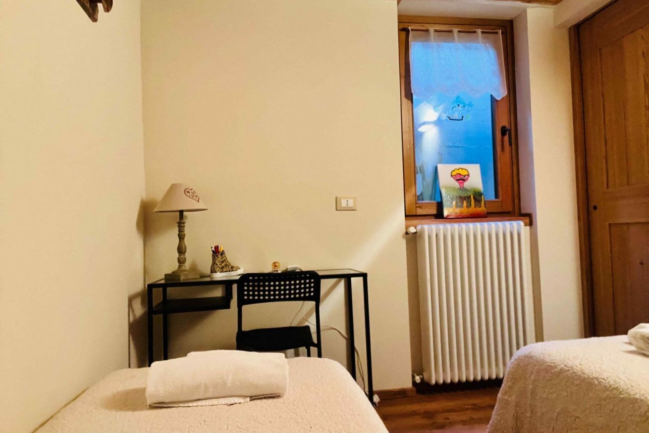 Un dormitorio con cama, escritorio con silla, ventana con vistas y radiador.