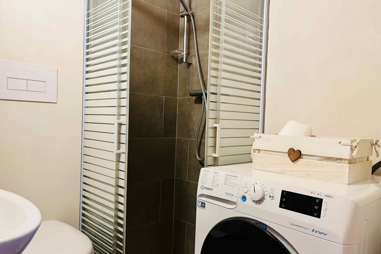 A bathroom with a washing machine, a toilet, and a shower enclosure.