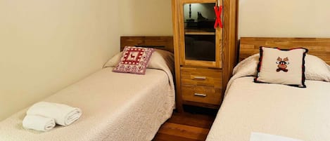 Een slaapkamer met twee bedden, een houten garderobe en een nachtkastje.