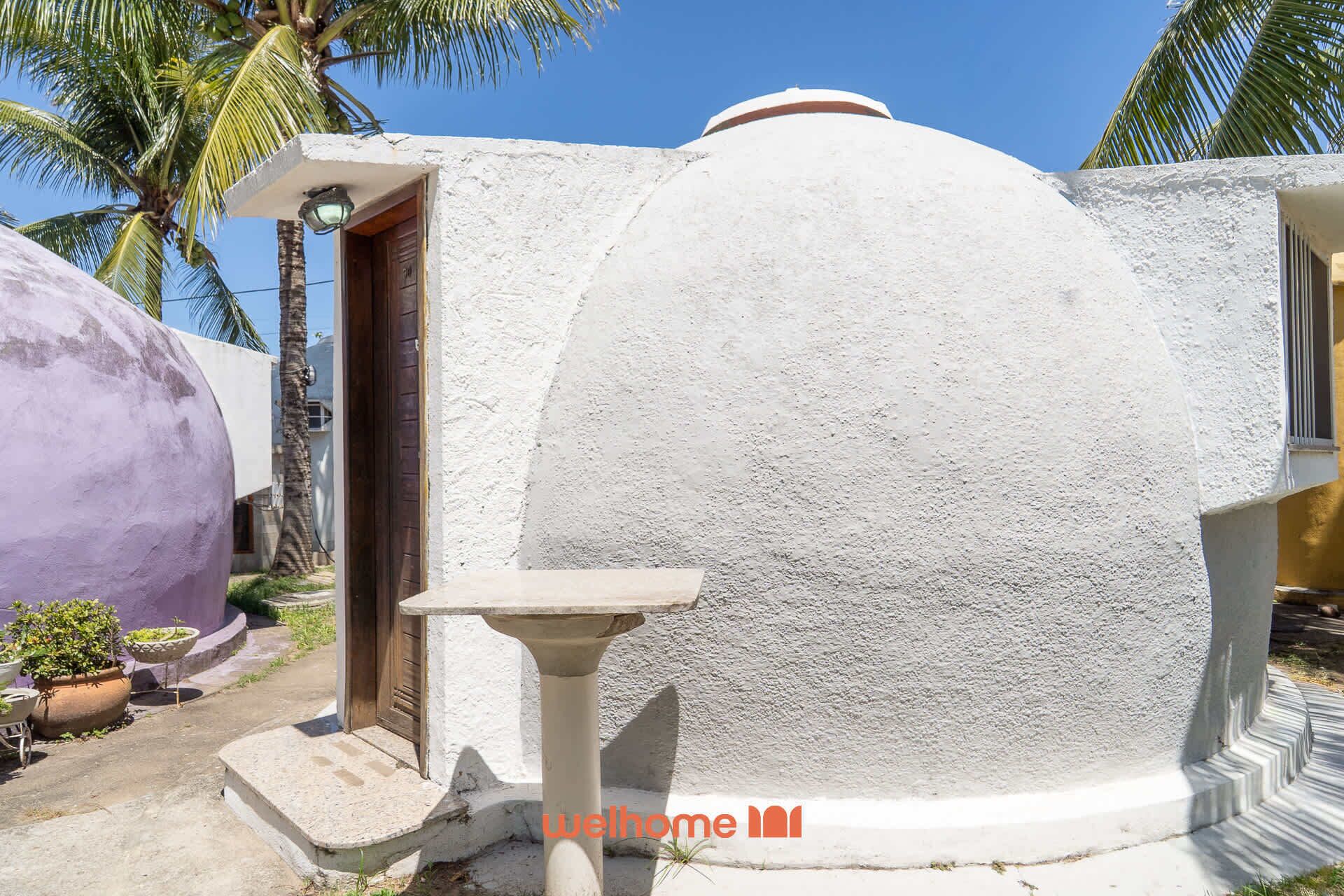 Un edificio blanco de forma abovedada, con una puerta y una pequeña mesa al frente.