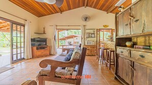 A spacious living area with a wooden bench, a television, and a kitchen area with bar stools. - Casa em Ubatuba a 10 minutos de carro da praia (Ubatuba)