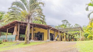 A rustic building with a covered porch, surrounded by lush greenery and palm trees. - Casa em Ubatuba a 10 minutos de carro da praia (Ubatuba)