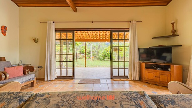 A living room with a television, a sofa, a coffee table, and a view through a glass door to a garden. - Casa em Ubatuba a 10 minutos de carro da praia (Ubatuba)