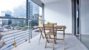 Un balcón con una mesa y sillas, vistas a la ciudad y una puerta de cristal.