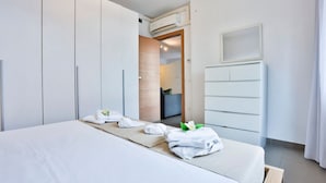 Habitación de hotel con cama, armario, escritorio y baño visible a través de una puerta abierta.