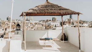 Una terraza en la azotea con una estructura de techo de paja, una banca y vistas de una ciudad muy poblada.