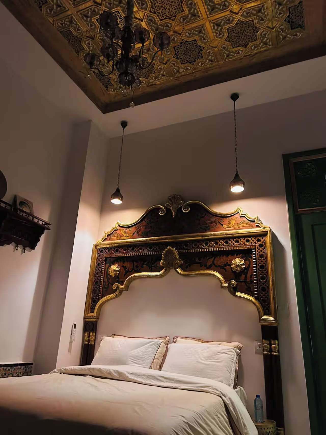 A bedroom with an ornate wooden headboard, a bed with white linens, and two pendant lights.