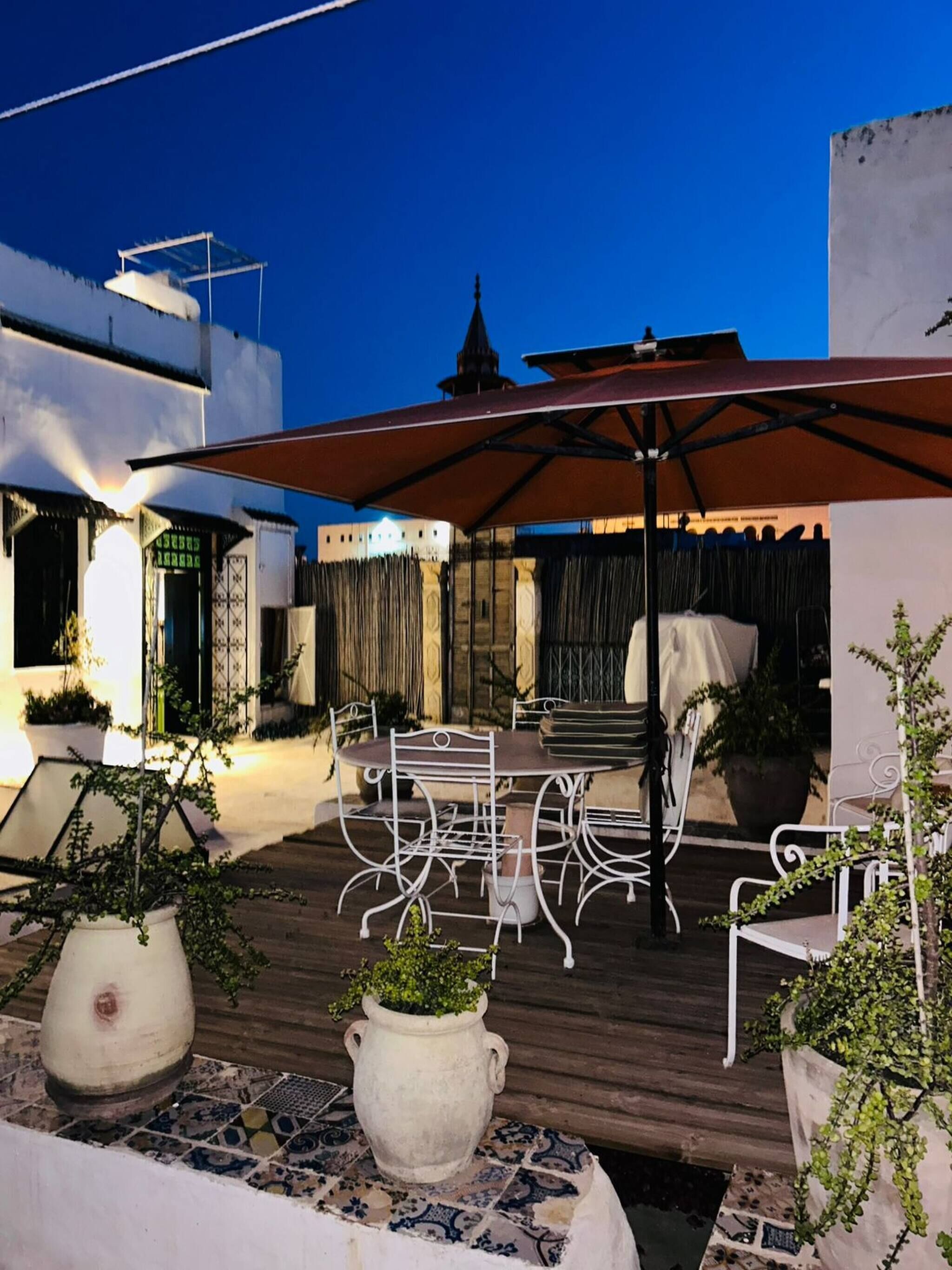 An outdoor patio with a table and chairs, potted plants, and a building in the background.