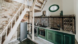 Una cocina con pared de piedra, una escalera de madera, lavadora y un armario verde.