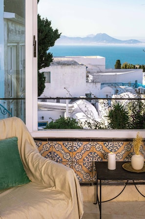 A balcony with a view of the sea and white buildings, a beige sofa, and a patterned tile backsplash. - Maison L'étoile de Sidi Bou Saïd - 360° Sea View (Sidi Bou Said)