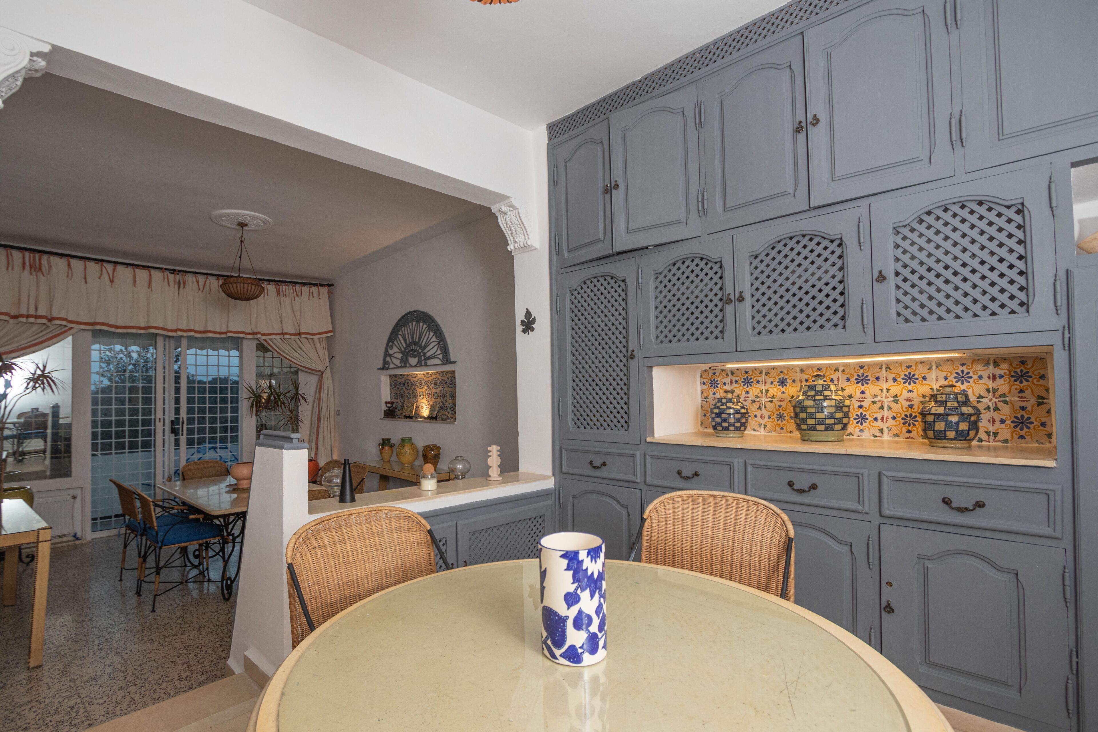 A dining area with a round table, wicker chairs, and a blue and white patterned mug.