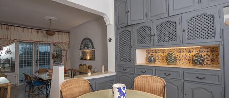 A dining area with a round table, wicker chairs, and a blue and white patterned mug.