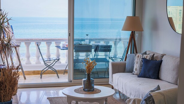 Un salon avec vue sur la mer, un canapé blanc, une table basse et une lampe.