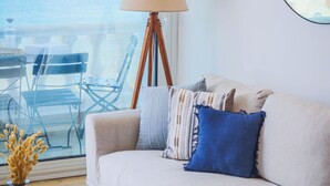 Un salon avec un canapé, une lampe, une table ronde et une vue sur la mer, visible à travers une grande fenêtre.