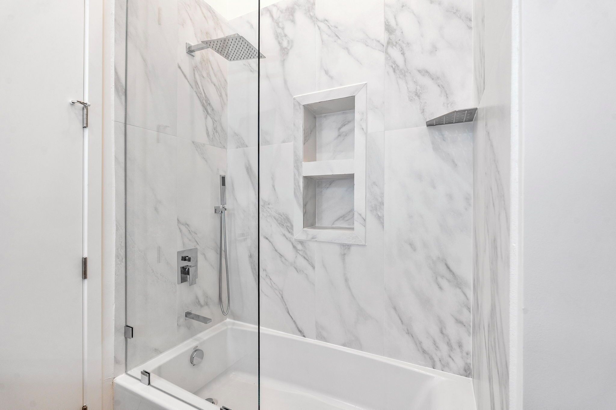 A modern bathroom with a glass-enclosed shower, marble walls, and a built-in shelf.