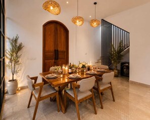 A dining area with a wooden table set for six, surrounded by chairs, with hanging pendant lights above. - 3BR Private Pool Villa in Berawa • Walk to Beach, Cafes & Finns (Bali)