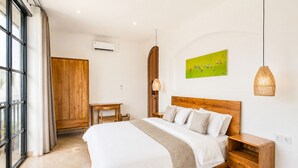 Een slaapkamer met een houten bed, een nachtkastje, een houten garderobe, een kleine tafel en een hanglamp.