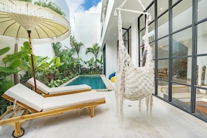 A modern indoor pool area with lounge chairs, a hanging macrame chair, and a large umbrella. - 3BR Private Pool Villa in Berawa • Walk to Beach, Cafes & Finns (Bali)
