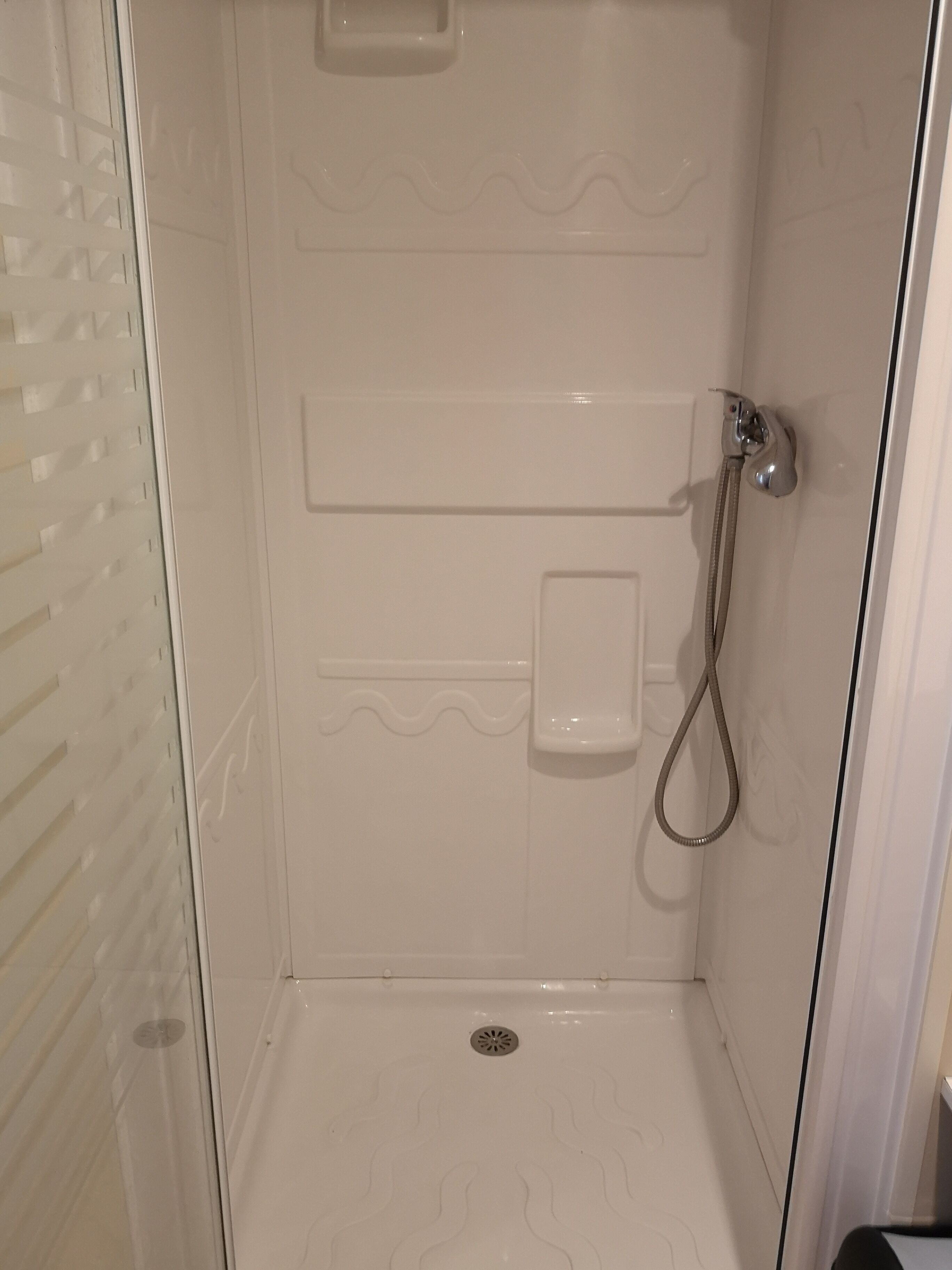 A shower area with a glass door, a showerhead, and a control panel.