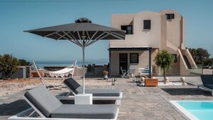 Una vila moderna amb piscina, gandules i cadira espanyola vora mar.