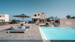 Zona de piscina al terrat amb gandules, ombrel·les i una vista despejada del mar.