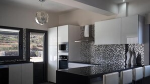 Cuina moderna amb una illa central, armaris blancs, un salvassecs negre i una finestra gran.