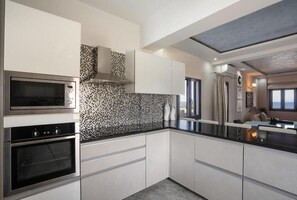 A modern kitchen with white cabinets, a black countertop, and a patterned backsplash. - Mythique Pool Residence - Oia Santorini (Oia)