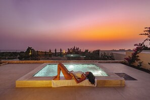Eine Person entspannt am Pool mit Blick auf einen Sonnenuntergang.