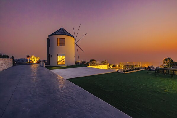 A modern house with a windmill, a paved patio, and a grassy area with outdoor furniture.