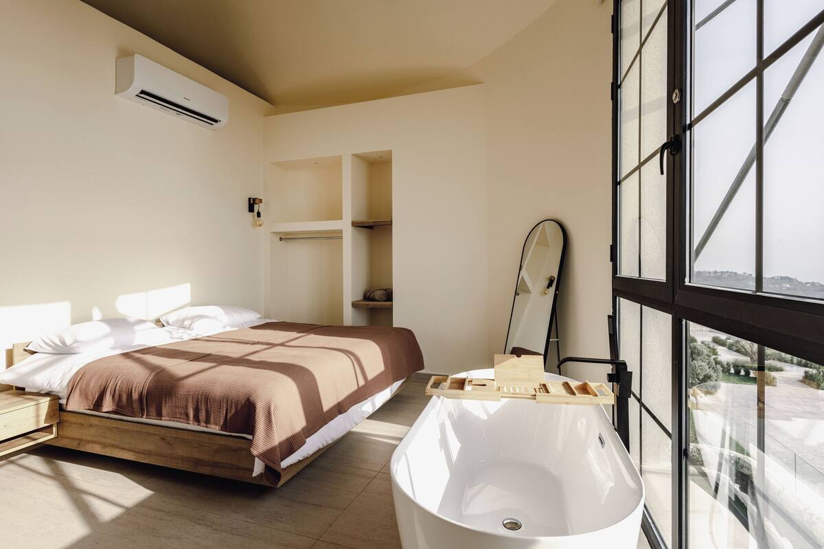 Une chambre moderne dotée d’un grand lit, d’une baignoire intégrée et d’une grande fenêtre donnant sur l’extérieur.