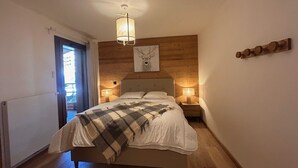 Un dormitori amb un llit, dues làmpades de nit, un capçal de llit de fusta, una obra d'art penjada a la paret i una porta que dona a una zona exterior.