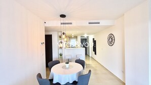 A modern dining area with a round table and chairs, a pendant light, and a clock on the wall. - Linnea Sol by Villas&You (Orihuela Costa)