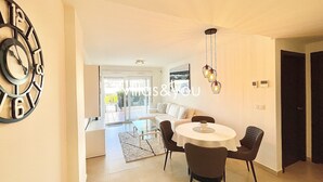 A modern living room with a dining area, a large wall clock, and a view through the glass door. - Linnea Sol by Villas&You (Orihuela Costa)
