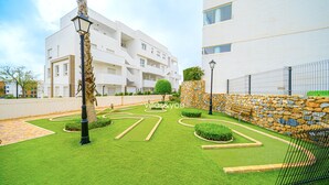 A well-maintained courtyard with manicured grass, a stone wall, and a modern building in the background. - Linnea Sol by Villas&You (Orihuela Costa)