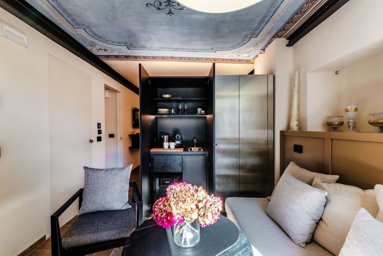 A modern interior with a sofa, a small table with a vase, and a kitchen area with cabinets and appliances.
