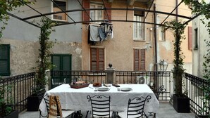 Un área de comedor al aire libre con una mesa preparada para cuatro personas, rodeada de sillas de metal y un mantel blanco.