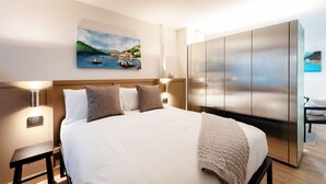 Una habitación de hotel con una cama grande, cabecera, mesitas de noche, armario y un cuadro en la pared.