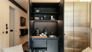 Una kitchenette compacta con cafetera, un lavamanos y estantes para guardar cosas.