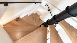 Una escalera de madera con barandilla negra y una lámpara en el techo.