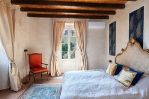 Una camera da letto con un letto, una sedia, una finestra con tende e un quadro appeso al muro.