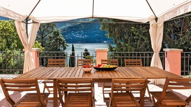 A wooden table with chairs and a bowl of fruit under a tent, overlooking a lake and hills. - Pink Villa - MyHomeinComo (Carate Urio)