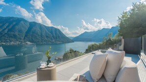 Eine Terrasse mit Blick auf einen See und Berge, ein Sofa und ein Tisch mit Tasse und Untertasse.