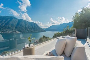 A terrace with a view of a lake and mountains, a sofa, and a table with a cup and saucer. - Villa Aurea - My Home in Como (Sala Comacina)
