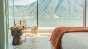 Ein Hotelzimmer mit großem Fenster, einem Bett, einem Sessel und einem kleinen Tisch mit einem Brotkorb.