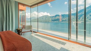 Ein Zimmer mit großem Fenster, einem Bett, einem Sessel und einem kleinen Tisch.