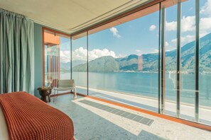 A room with a large window, a bed, a chair, and a small table. - Villa Aurea - My Home in Como (Sala Comacina)