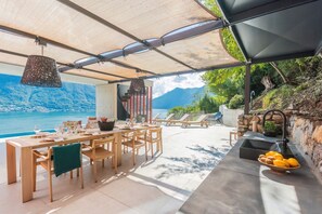 Un espace extérieur abrité, aménagé pour les repas, avec vue sur la mer, du mobilier en bois et un mur en pierre.